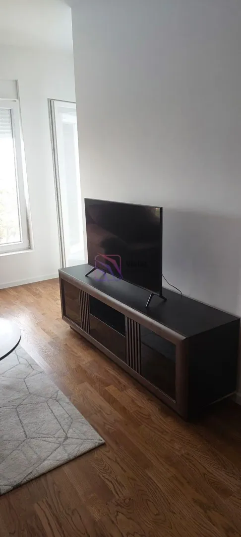 Dnevni boravak sa komodom za televizor i drvenim podom.