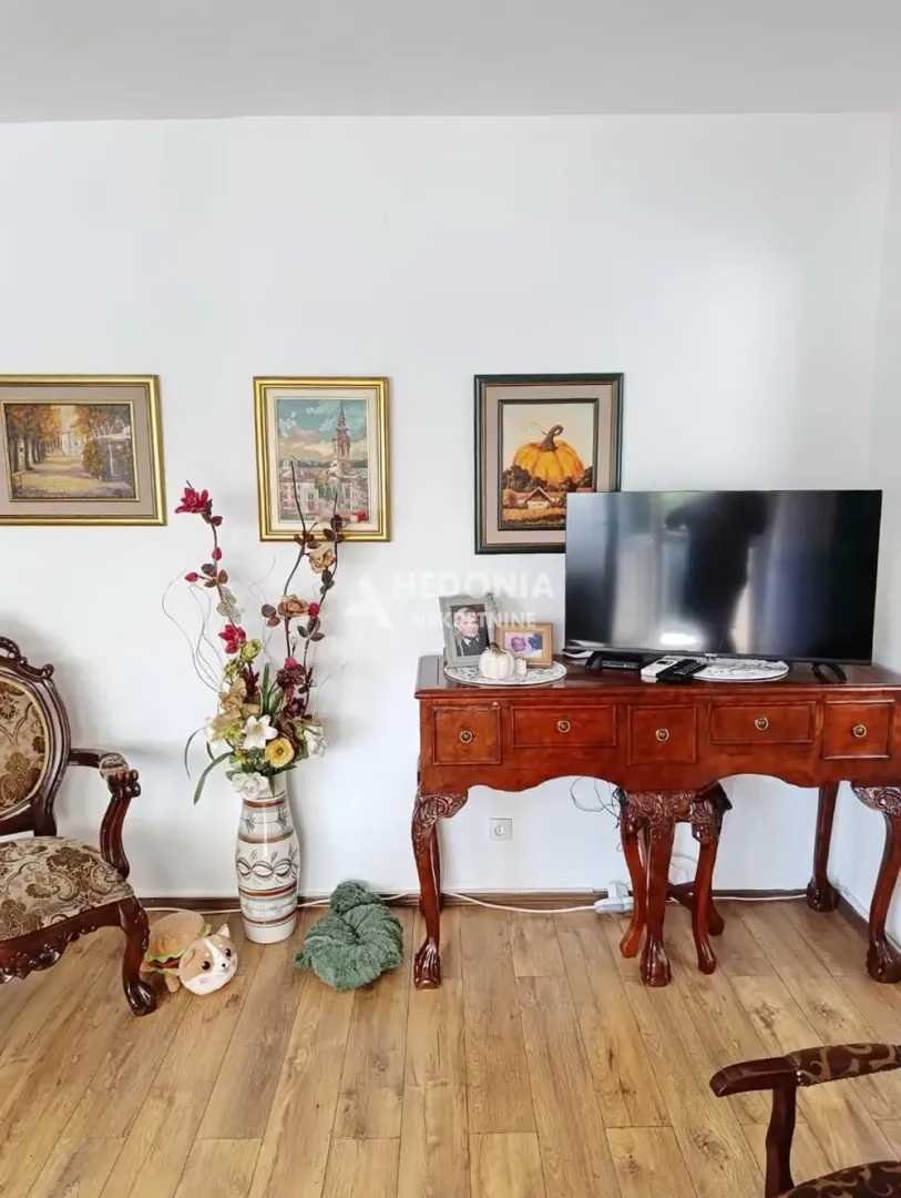Dnevna soba sa drvenom komodom, televizorom i slikama na zidu.