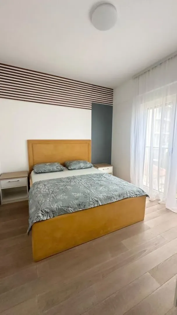 Svjetla spavaća soba sa bračnim krevetom, noćnim stočićima i balkonskim vratima.