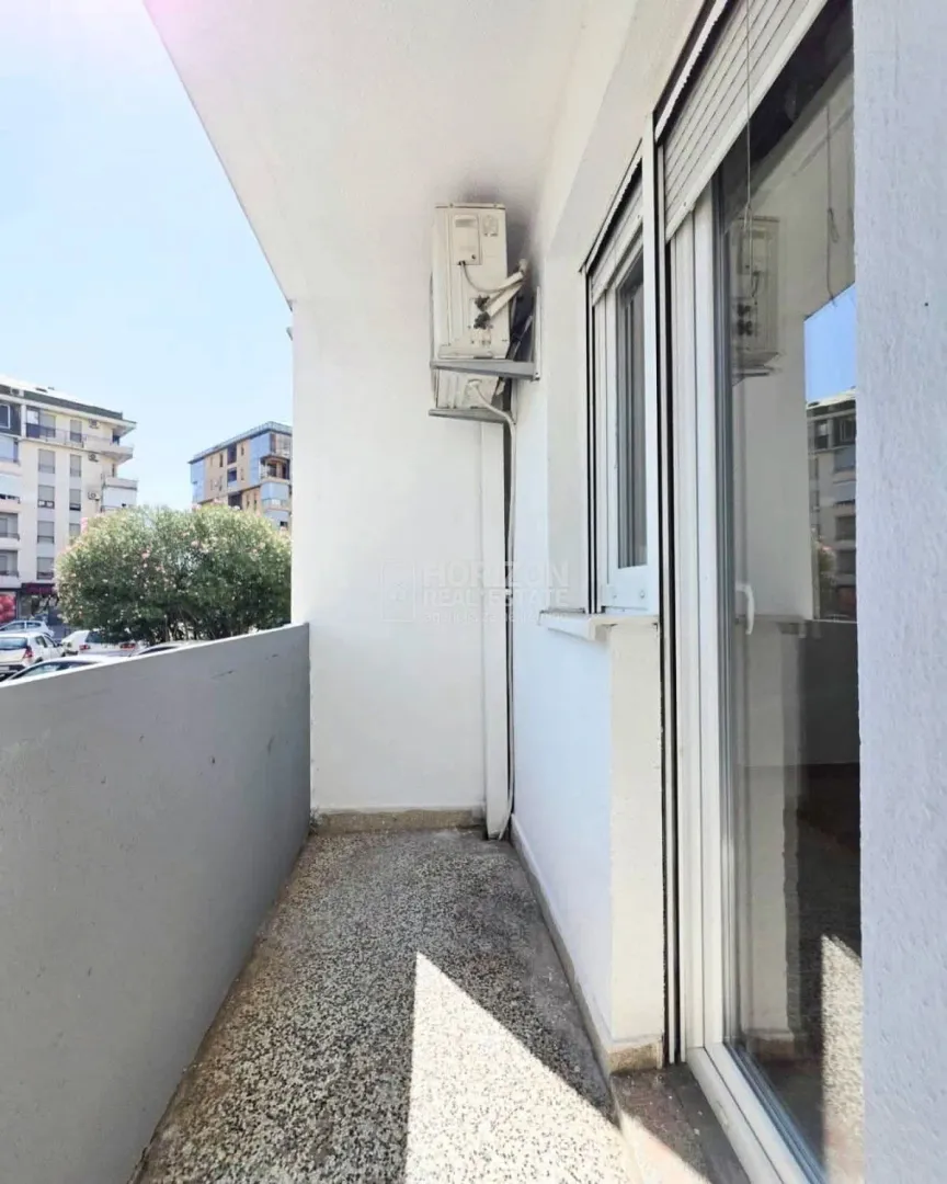 Smaller bright balcony with an external air conditioning unit and a view of surrounding buildings.