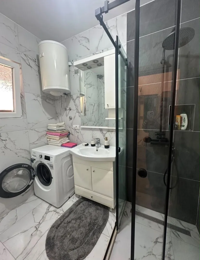 Moderne kupatilo sa tuš kabinom, umivaonikom i veš mašinom.