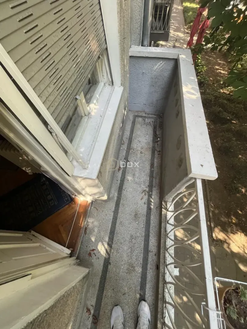 Pogled odozgo na balkon sa metalnom ogradom i prozorom sa roletnama.