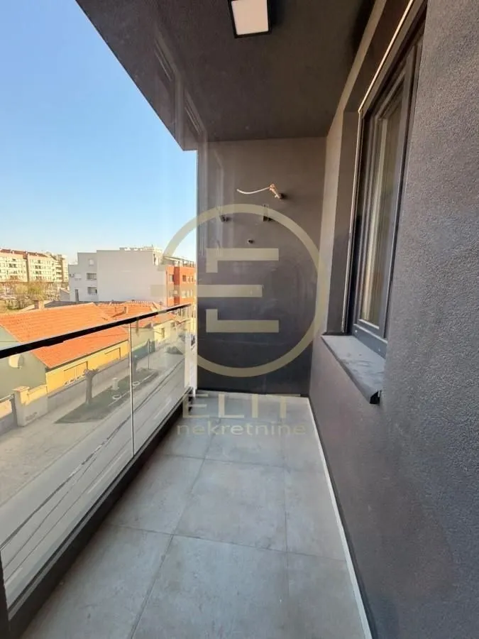 Nenamešten balkon sa staklenom ogradom i pogledom na okolne zgrade.