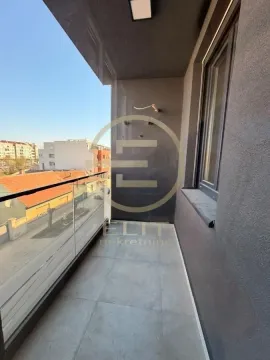 Nenamešten balkon sa staklenom ogradom i pogledom na okolne zgrade. - image 7
