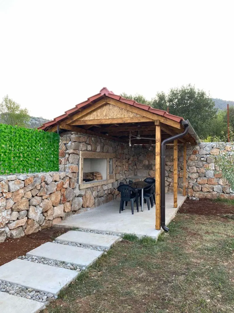 Covered gazebo with a built-in barbecue and seating set in the yard.
