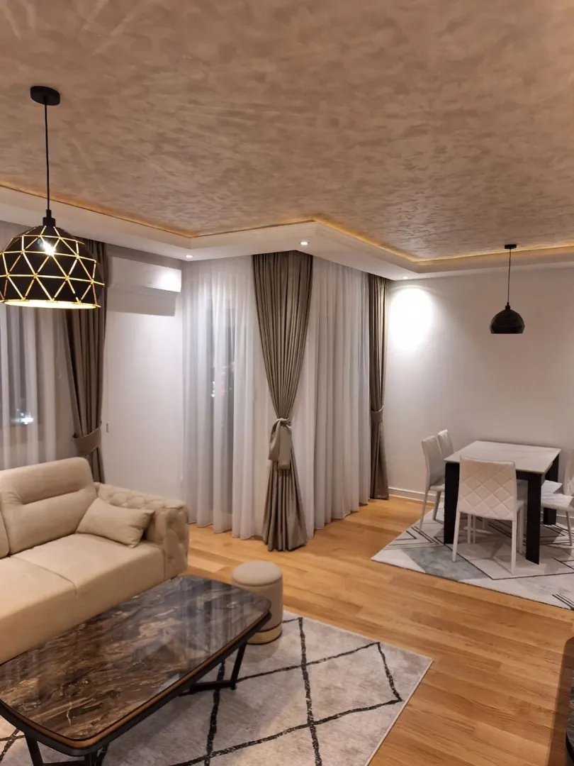 Svijetla i moderno uređena dnevna soba sa trpezarijom i elegantnim osvjetljenjem.
