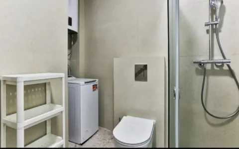 Bathroom with a shower cabin, toilet, and washing machine. - image 5