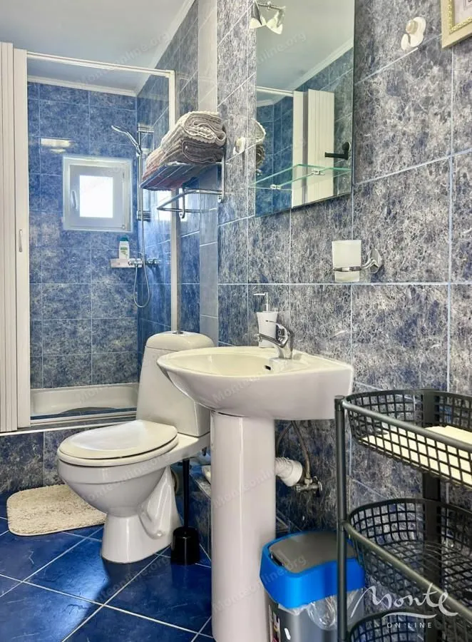 Kupatilo obloženo plavim pločicama sa tuš kabinom, umivaonikom i wc šoljom.