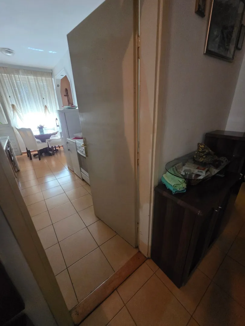 Pogled iz hodnika na kuhinju sa trpezarijskim stolom i prozorom.