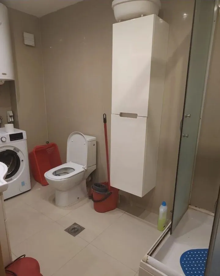 Manje uredno kupatilo sa WC šoljom, tuš kabinom i veš mašinom.