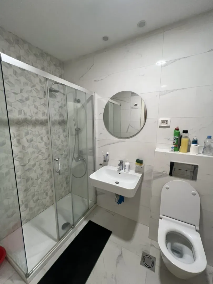 A modern bathroom with a glass shower, a sink, and a mirror.