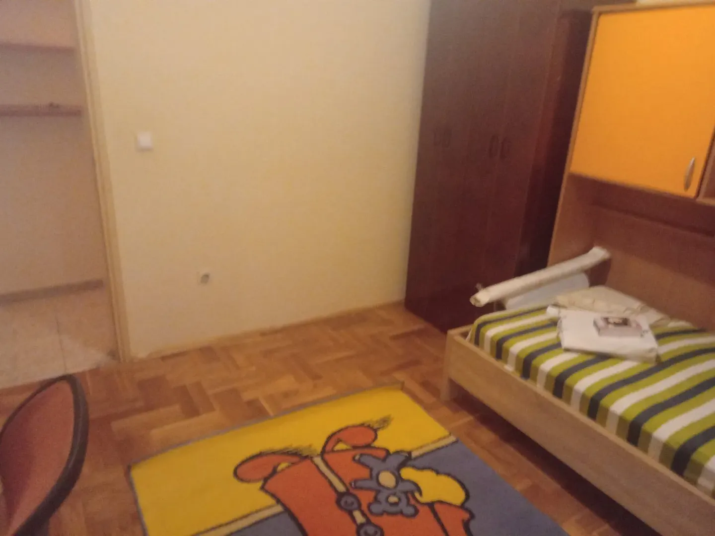 Dječija soba sa krevetom, ormarom i šarenim tepihom.
