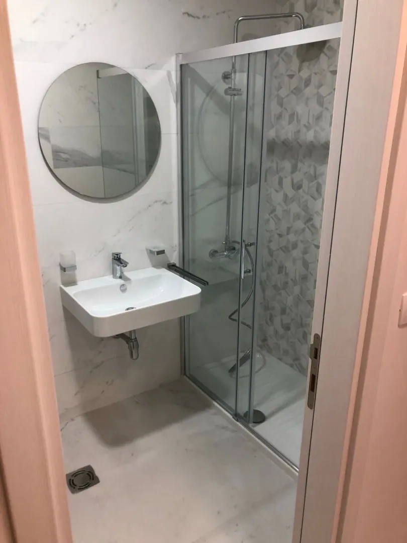Moderne kupatilo sa umivaonikom, tuš kabinom i okruglim ogledalom.