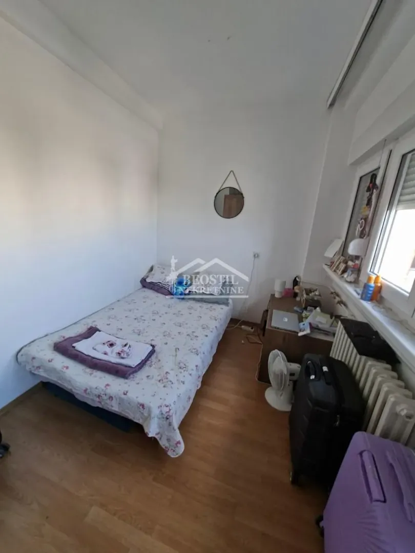 Manja spavaća soba sa krevetom i radnim stolom pored prozora.