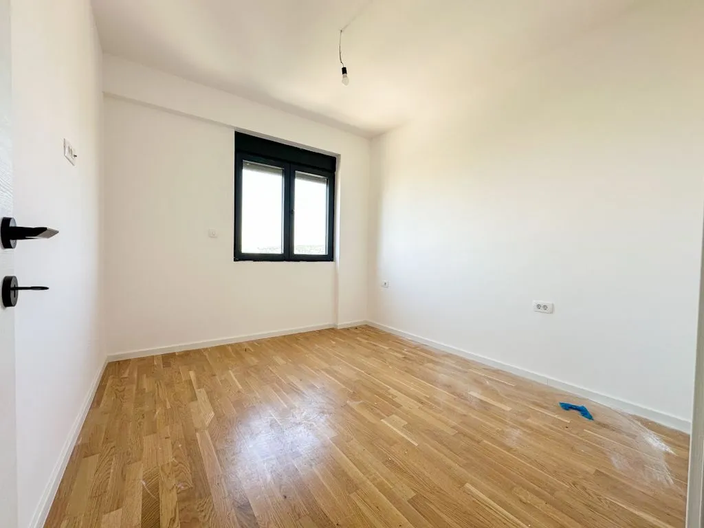 Prazna soba sa parketom i bijelim zidovima.