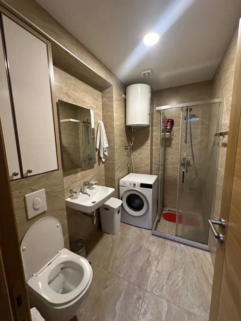 Kupatilo opremljeno tuš kabinom, umivaonikom, WC šoljom i mašinom za veš.