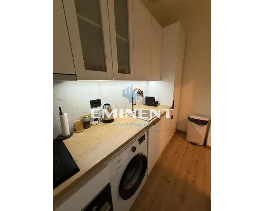 Small kitchen with white cabinets, wooden countertop and built-in washing machine.