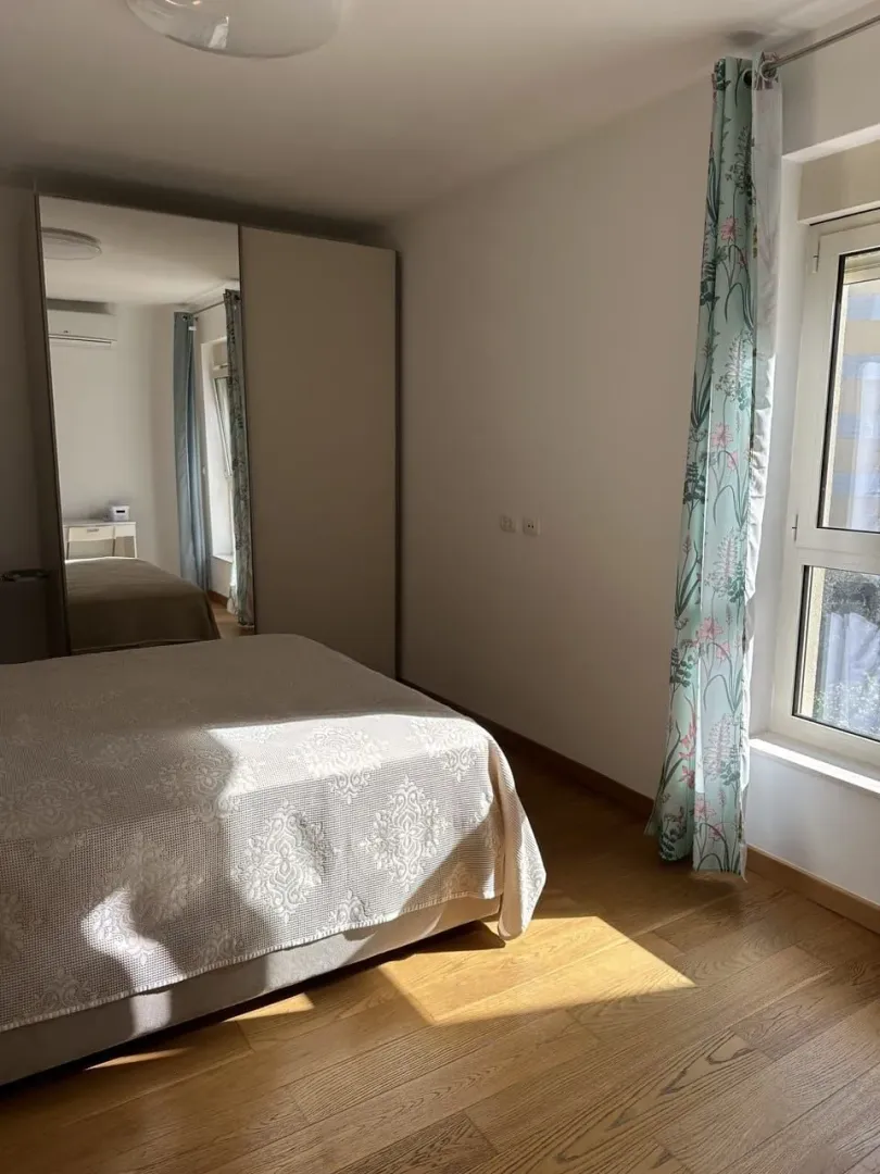 Spavaća soba sa bračnim krevetom, velikim plakarom i prozorom sa zavjesama.