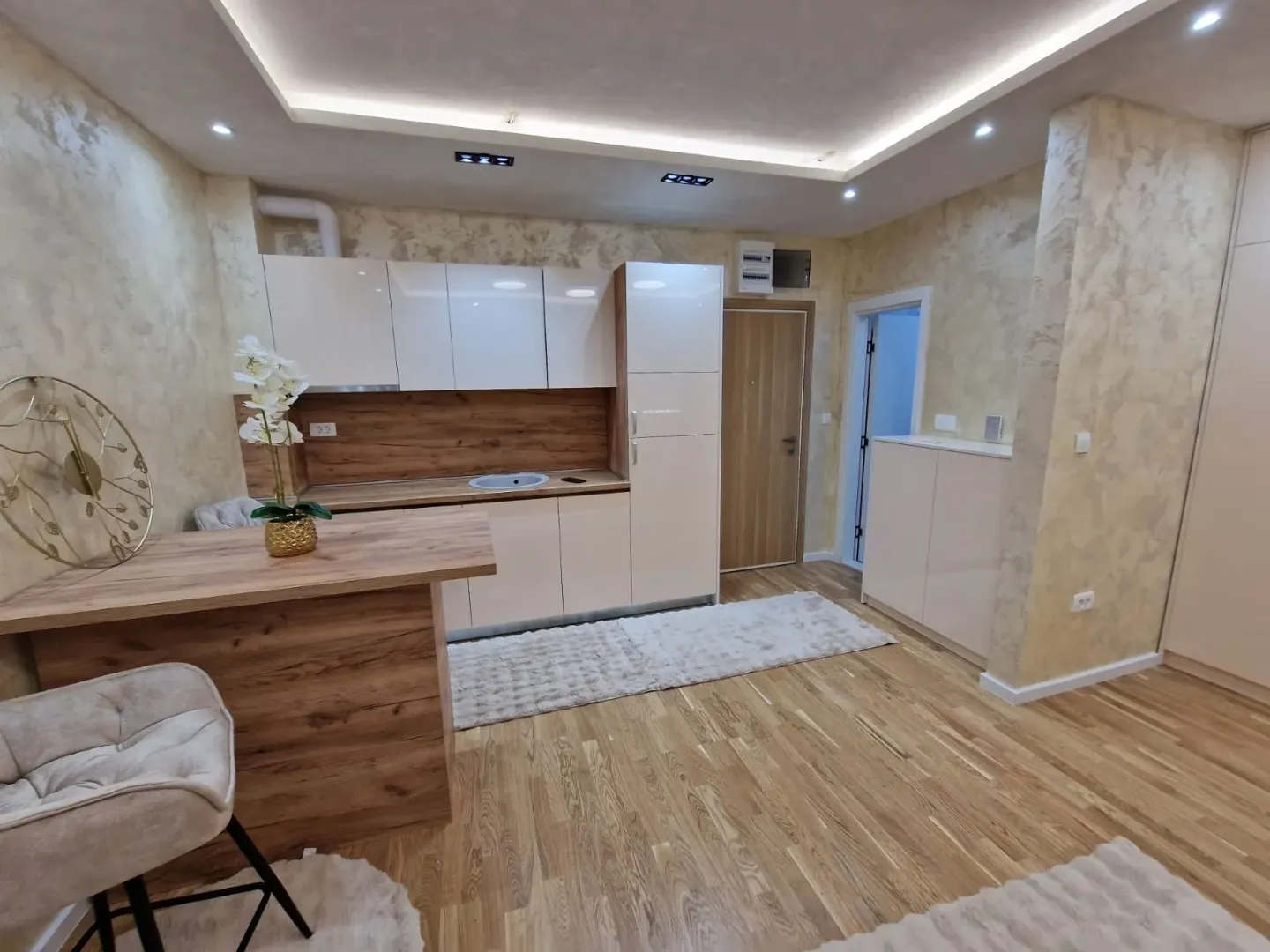 Moderna kuhinja sa bijelim i drvenim elementima i šankom.