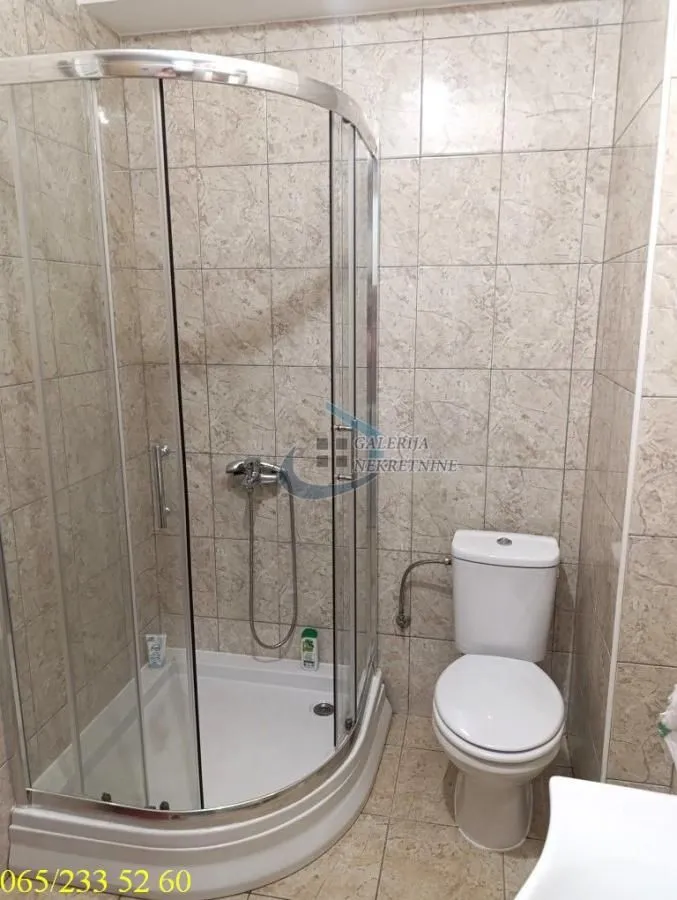 Kupatilo sa tuš kabinom i toaletom, obloženo keramičkim pločicama.