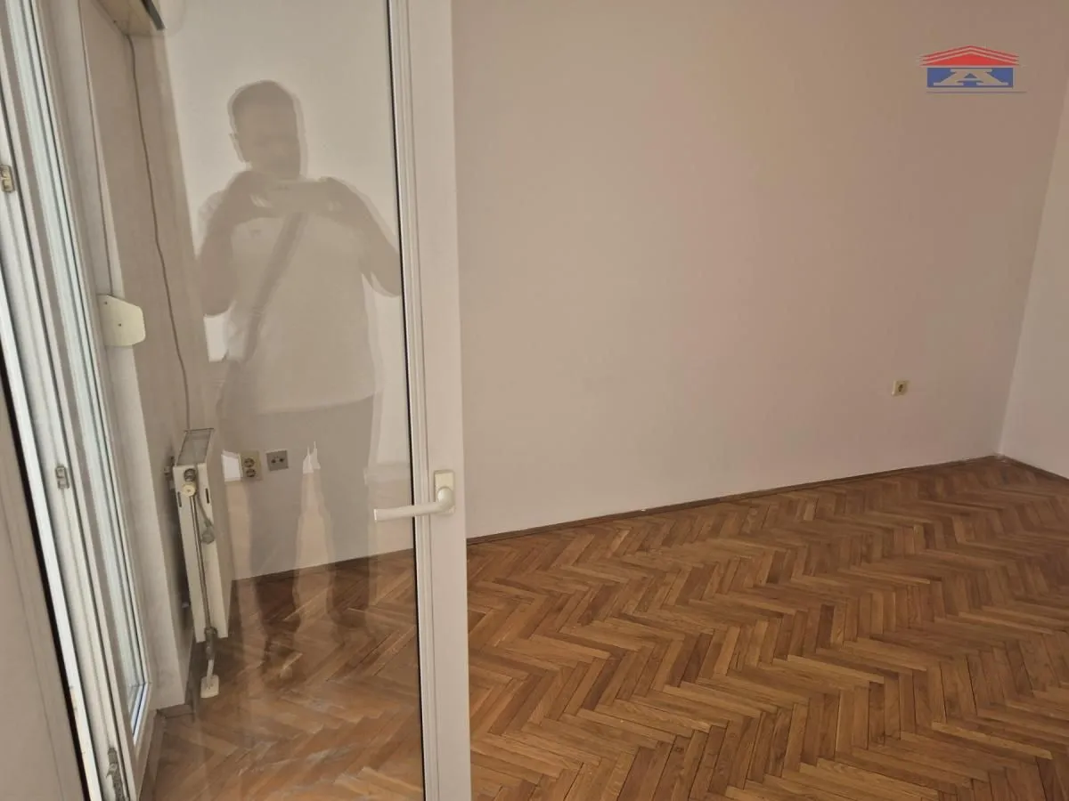 Prazna soba sa parketom i balkonskim vratima.