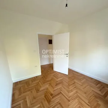 Prazna soba sa parketom i otvorenim vratima prema hodniku. - image 3