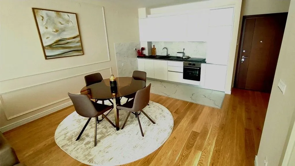 Living room with a dining area and built-in kitchen in light tones.