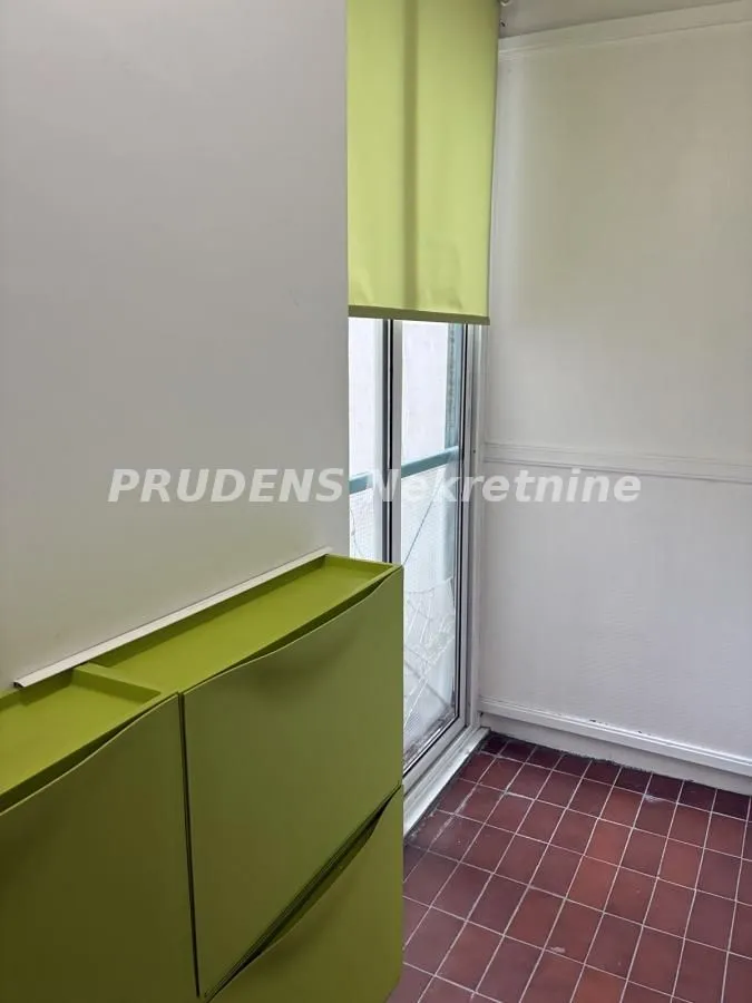 Zastakljeni balkon sa zelenim ormarićem i roletnama.