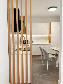 Moderna bijela kuhinja sa drvenim letvama i trpezarijskim stolom. - image 9