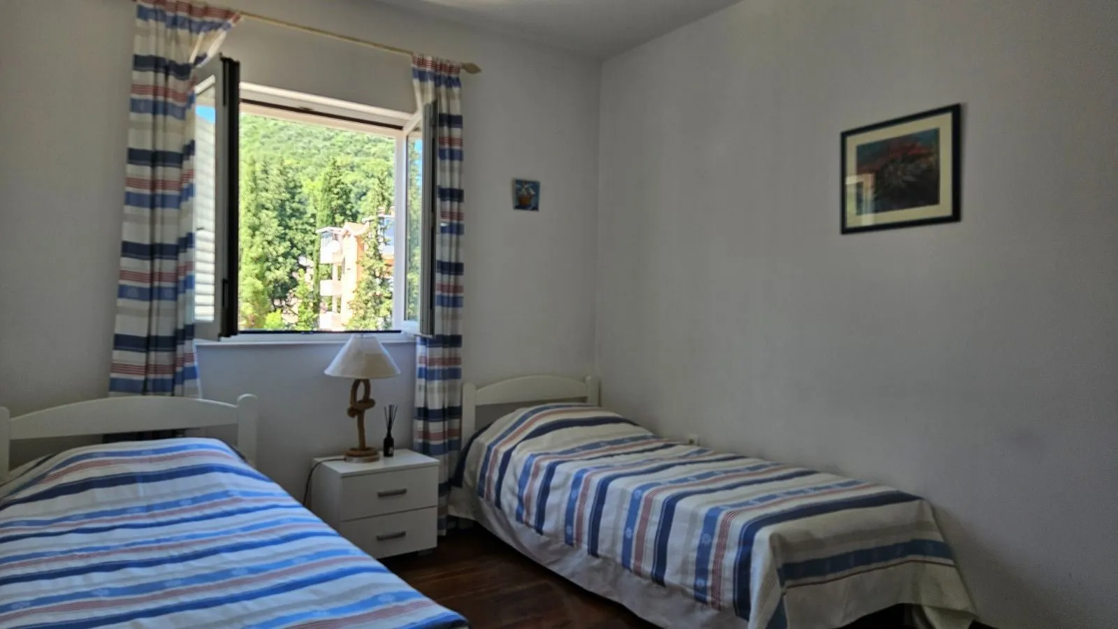 Spavaća soba sa dva kreveta i prozorom sa pogledom na zelenilo.