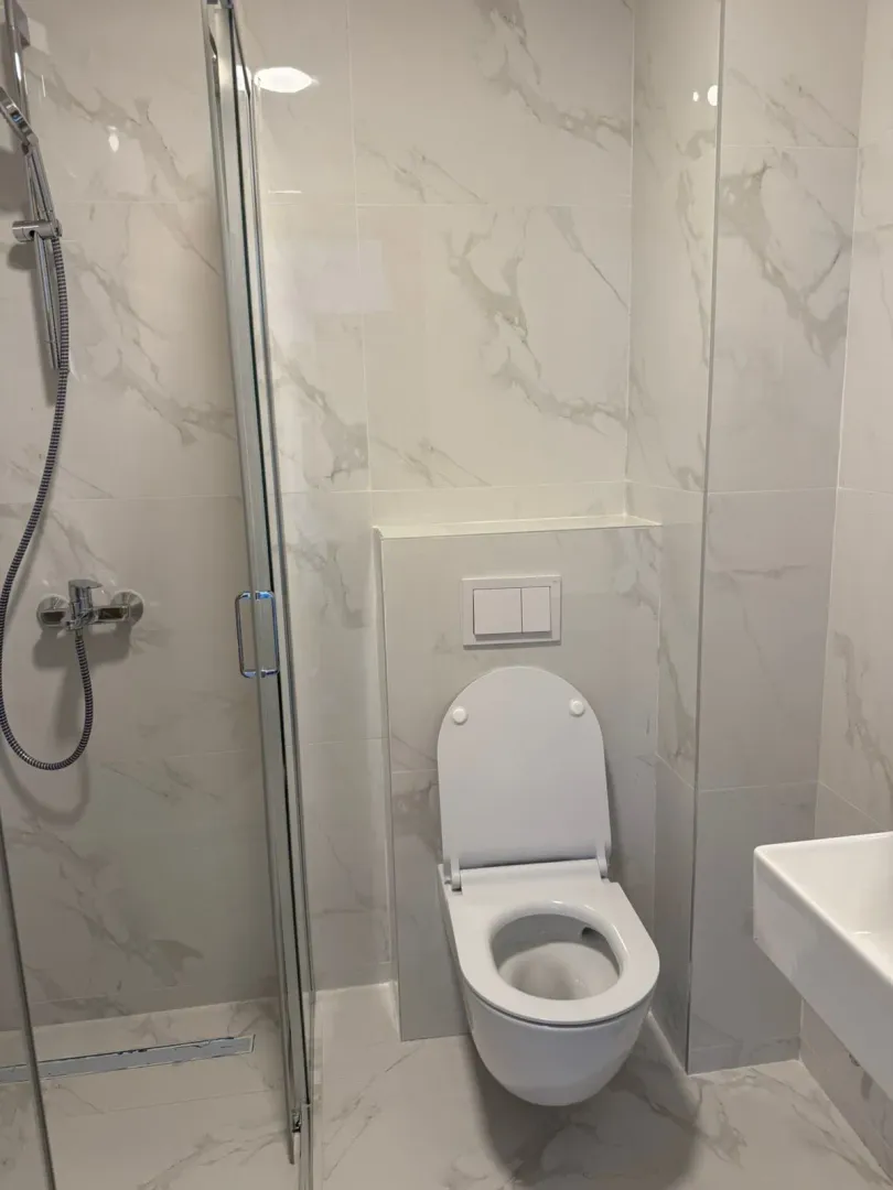 Moderne kupatilo sa tuš kabinom i ugradnom wc šoljom obloženo mermernim pločicama.