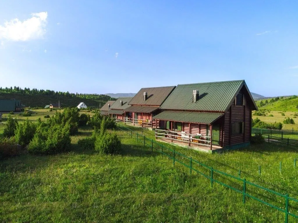 Pogled na drvene vikendice sa uređenim dvorištem i ogradom.