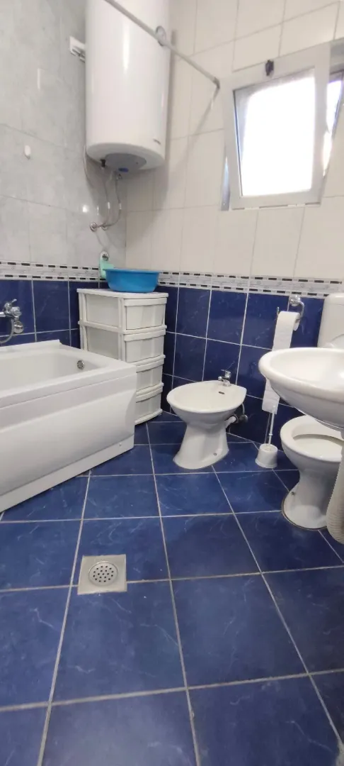 Small bathroom with blue tiles, bathtub, washbasin, toilet, and bidet.