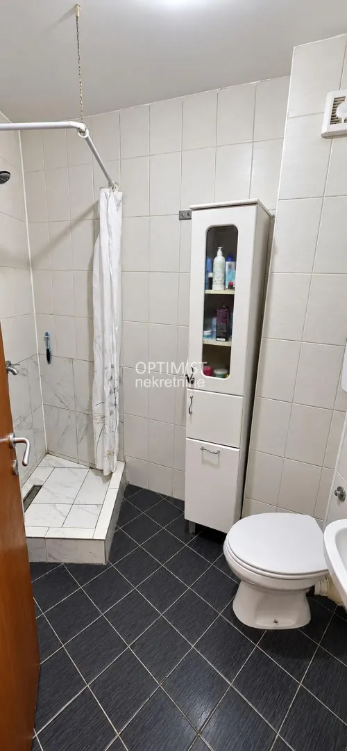Kupatilo sa tuš kabinom, toaletom i belim ormarićem.