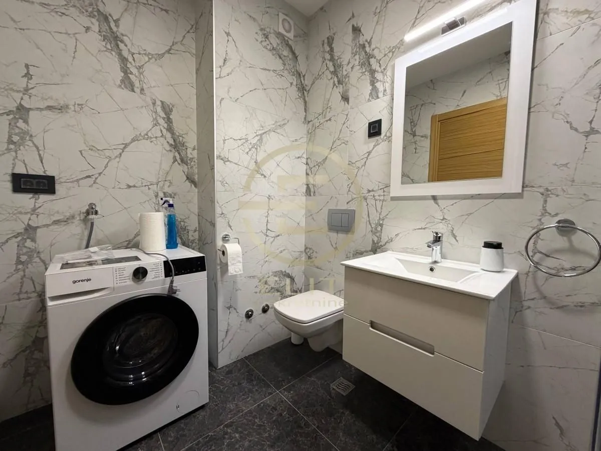 Modern bathroom with marble tiles, vanity, toilet, and washing machine.