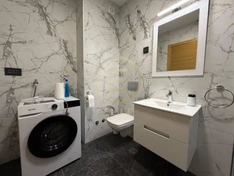 Modern bathroom with marble tiles, vanity, toilet, and washing machine. - image 10