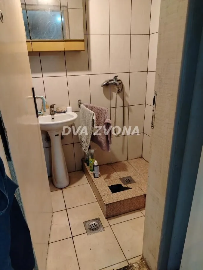 Manje kupatilo sa umivaonikom i tuš kabinom sa pločicama.