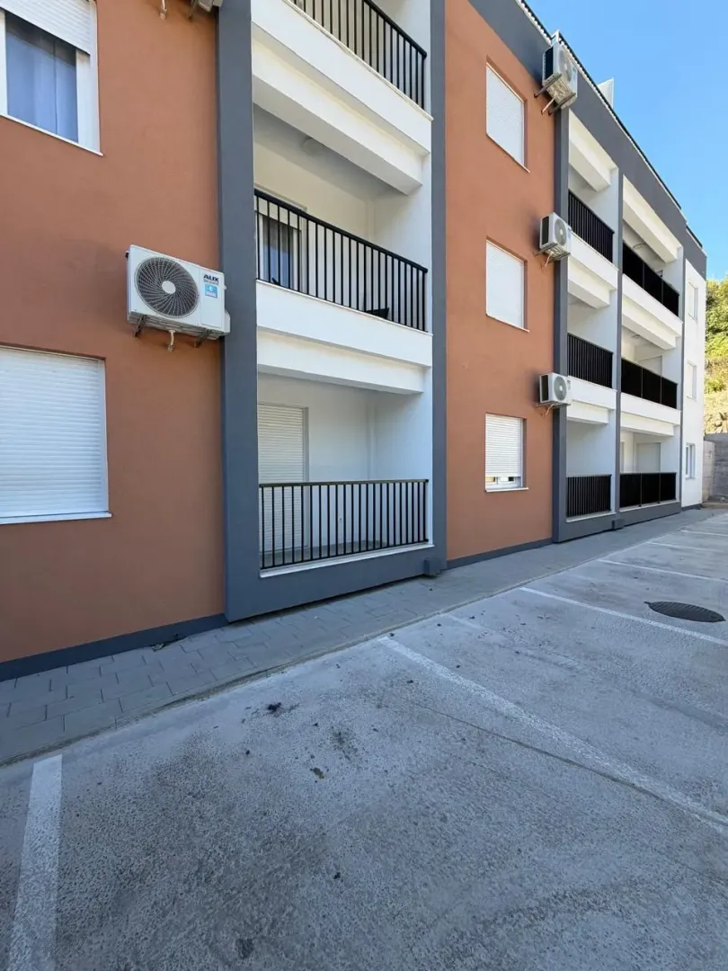 Eksterijer moderne stambene zgrade sa terasama i parking prostorom.