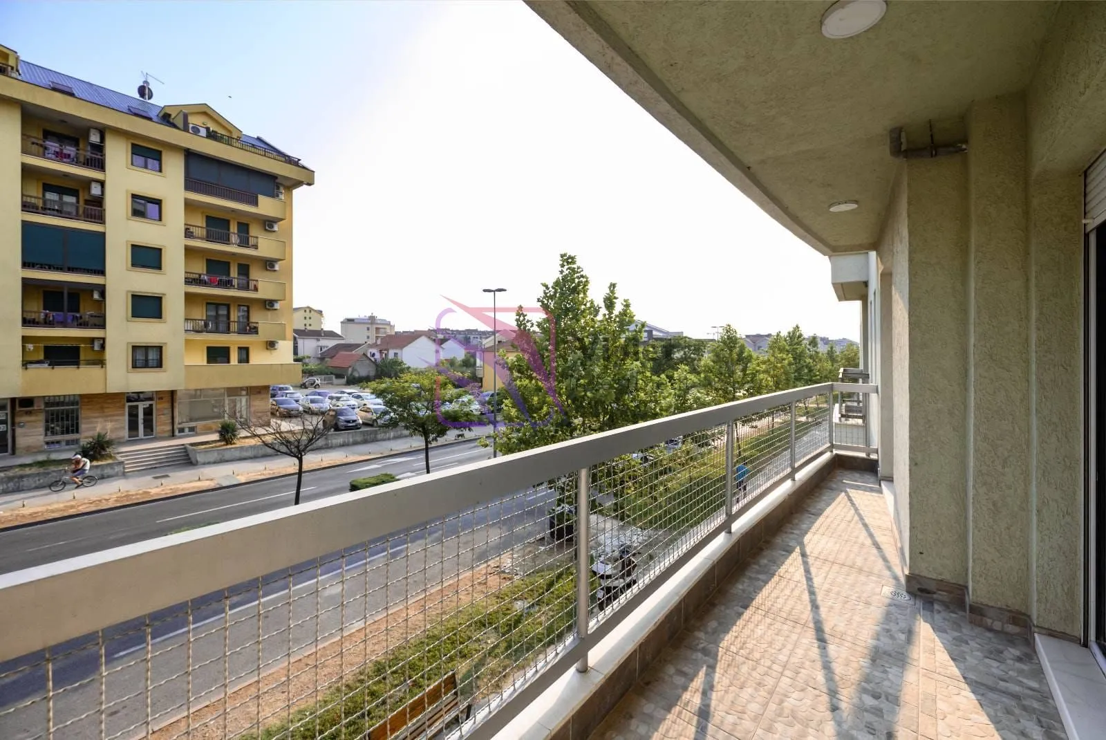 Spacious tiled balcony with a metal railing and a view of the street and surrounding buildings.