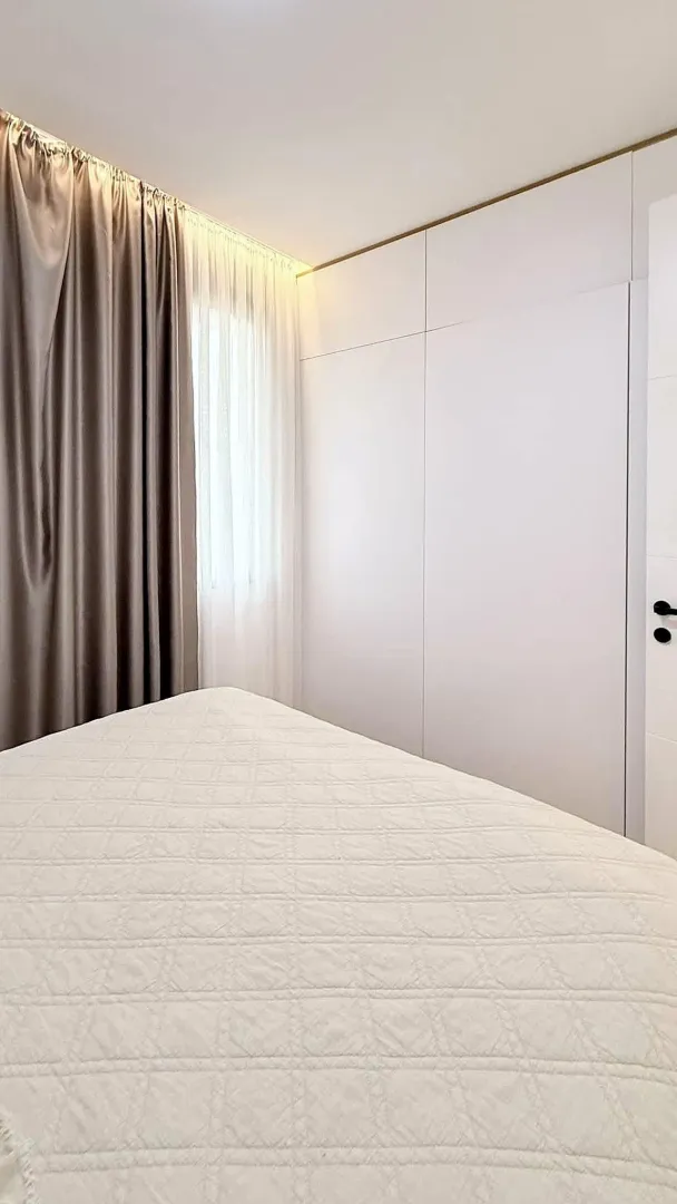 Bedroom with a double bed, built-in wardrobe, and a window with curtains.