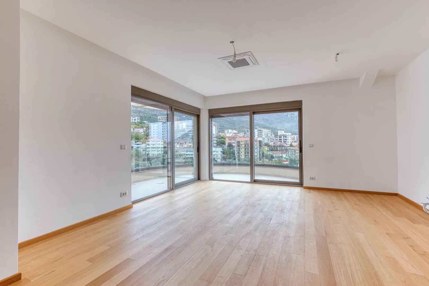 Empty bright room with wooden flooring and large glass sliding doors.