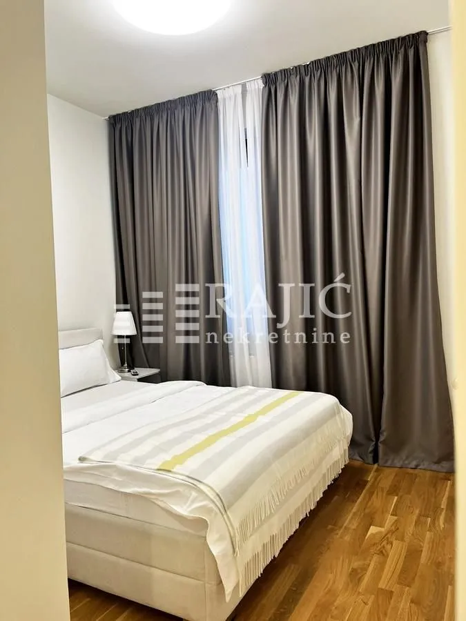 Furnished bedroom with a double bed and dark curtains.