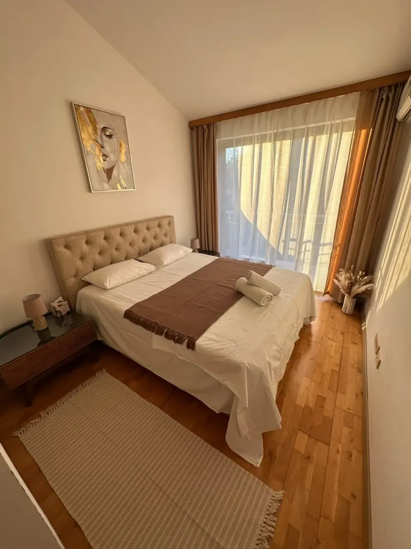Uređena spavaća soba sa bračnim krevetom, drvenim podom i izlazom na balkon.