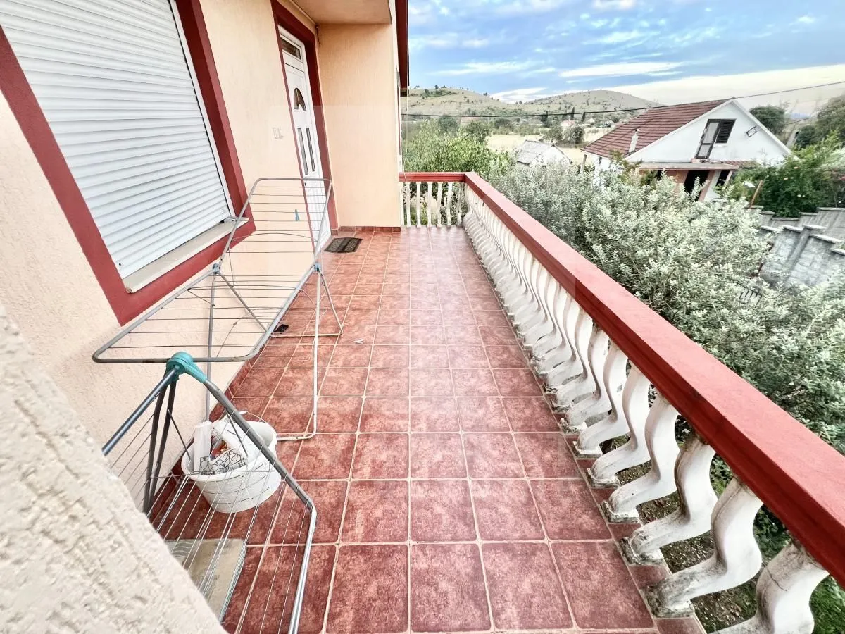 Prostrani popločani balkon sa ogradom i pogledom na okolinu.