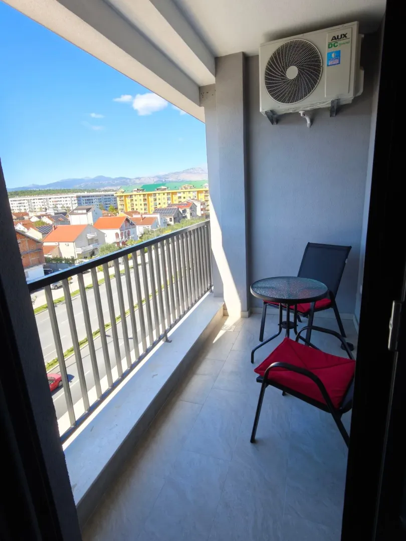Small furnished balcony with a table, chairs, and an air conditioning unit.
