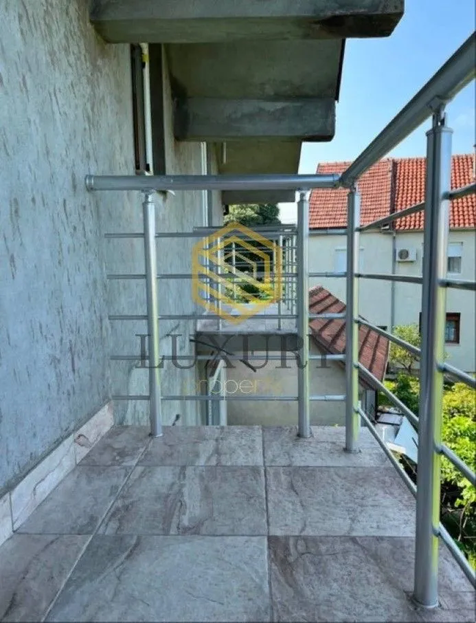 Popločani balkon sa metalnom ogradom i pogledom na okolne zgrade.