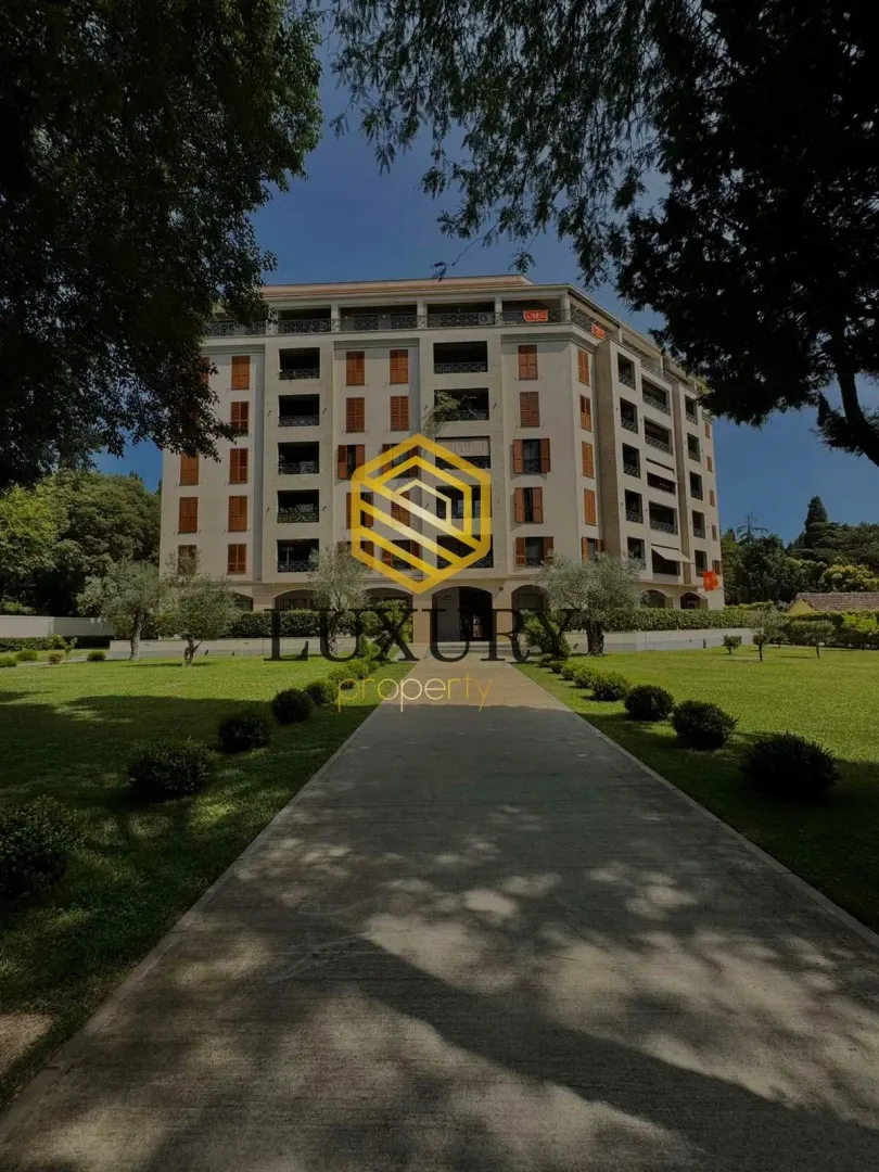 Pogled na fasadu stambene zgrade sa uređenim dvorištem i stazom.