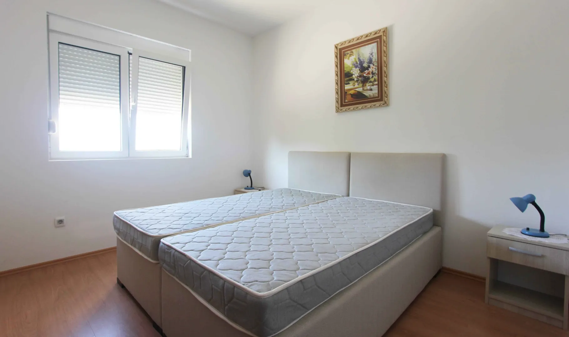 Jednostavno namještena spavaća soba sa dva spojena kreveta i noćnim stolovima.