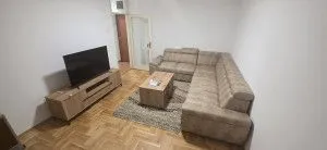 Dnevna soba sa ugaonom garniturom, televizorom i parketom na podu.