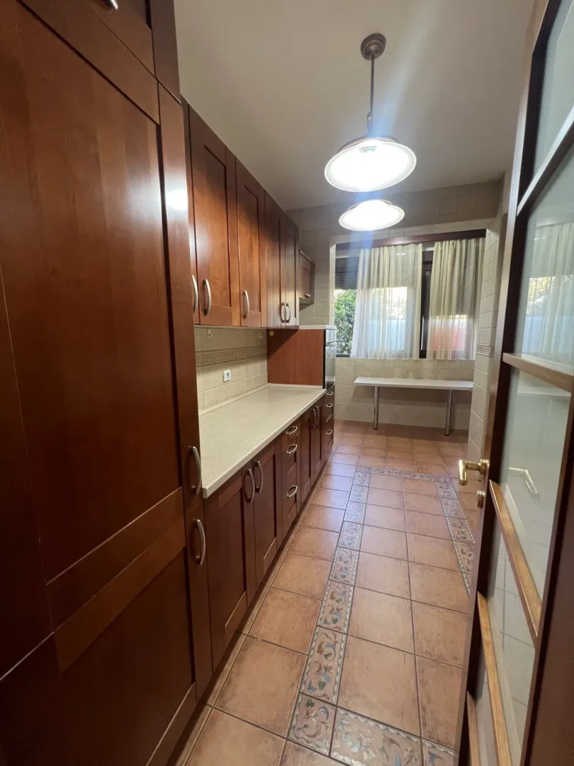 A long kitchen with wooden cabinets and tiled flooring.
